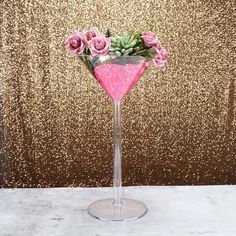 a pink cocktail glass filled with roses and succulents in front of a gold glitter backdrop