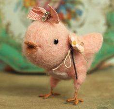 a small pink bird with a bow on its head is standing in front of a pillow