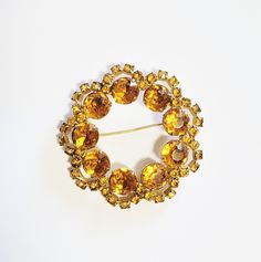 "Lovely, large gold rhinestone brooch in the shape of a circle or wreath. The gold metal setting is inset with prong set gold rhinestones.  The rhinestones are two different sizes. The large rhinestones are located in the inner part of the brooch pin. The location of the smaller rhinestones has the effect of adding dimension to the beautiful brooch. The brooch is in mint condition, with all rhinestones clear and present. The pin of the clasp is slightly bent.  Not quite 2 1/2\" in diameter. Plea Gold Wedding Brooch, Gold Round Brooches For Wedding, Gold Round Costume Jewelry Brooches, Vintage Gold Brooches With Rhinestones, Gold Retro Wedding Brooches, Vintage Gold Round Brooches, Vintage Gold Brooch, Gold Rhinestone, Rhinestone Brooches