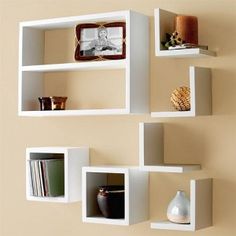 several white shelves are arranged on the wall with books and vases in front of them