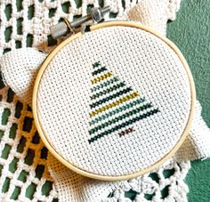 a cross stitch christmas tree ornament hanging from a hoop on a crochet doily