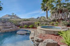 an outdoor swimming pool surrounded by palm trees and rocks with a hot tub in the middle