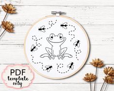 a cross stitch pattern with a frog and bees in the center on a white wooden background