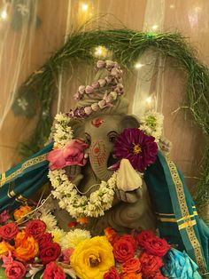 an elephant statue with flowers around it's neck sitting in front of a wreath