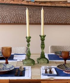 a table set with place settings and two candlesticks on top of each other