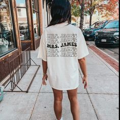 a woman walking down the sidewalk wearing an anti social wives club shirt on her back