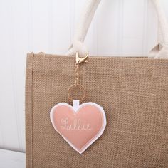 a pink heart shaped keychain hanging from a burlocked tote bag