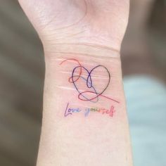 a small wrist tattoo with two hearts and the words love yourself written in multicolored ink