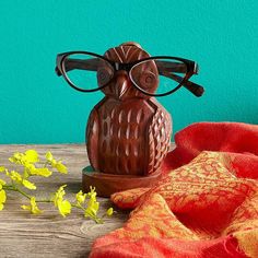 an owl figurine wearing glasses on top of a wooden table next to yellow flowers