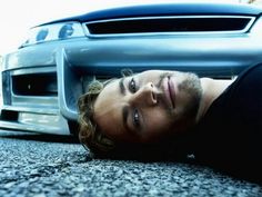 a young man laying on the ground next to a car with his head under it