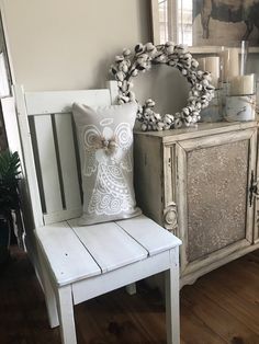 a white chair sitting next to a wooden cabinet with a pillow on top of it