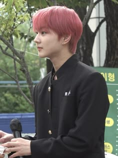 a young man with red hair is holding a microphone and standing in front of a tree