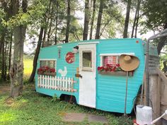 a blue trailer parked in the woods with flowers on it's side and a white picket fence