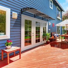 an outdoor deck with umbrellas and chairs next to a blue house on a sunny day