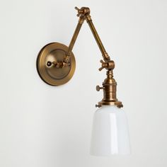 an antique brass wall light with a white glass shade on the arm and one bulb