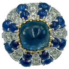 This 1950s European 18k gold cocktail ring features a central no heat sugarloaf cabochon sapphire which weighs approximately 3.5 carats and approximately 1 carat of diamonds. The smaller sapphires which adorn the ring weigh approximately 2 carats. Luxury Sapphire Ring With Cabochon, Luxury Blue Round Cabochons, Luxury Blue Cabochons For Anniversary, Fine Jewelry Domed Gemstone Cabochons, Domed Gemstone Cabochons Fine Jewelry, Classic Blue Gemstone Cabochons, Formal Domed Cabochon Sapphire Ring, Formal Cabochon Sapphire Ring, Formal Fine Jewelry Domed Cabochons