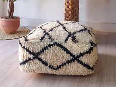 a white and black ottoman sitting on top of a wooden floor next to a potted plant