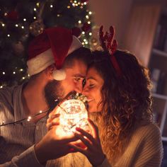 a man and woman are kissing in front of a christmas tree with lights on it