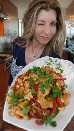 a woman holding a plate with chicken and veggies on it