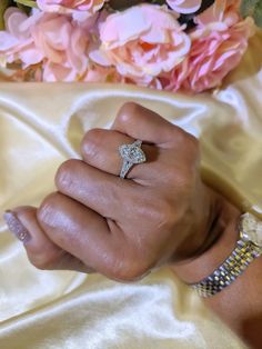 a woman's hand with a diamond ring on top of her left hand and pink flowers in the background