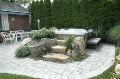 an outdoor hot tub surrounded by rocks and plants in front of a brick patio area