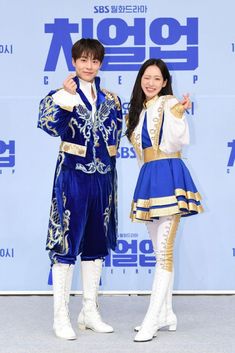 two people standing next to each other in front of a blue and white wall with words written on it