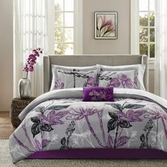 a bed covered in purple and white comforter next to a vase with flowers on it