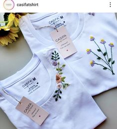 two white t - shirts with flowers on them and price tags attached to the front