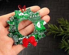 a hand holding a green christmas ornament with red bows on it's head