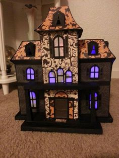 a doll house with blue lights on the front and side windows, sitting on a carpeted floor