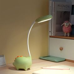 a desk lamp sitting on top of a wooden table next to a book and pen