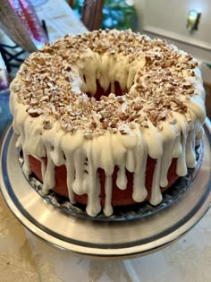 a bundt cake with white icing and nuts on top sitting on a plate