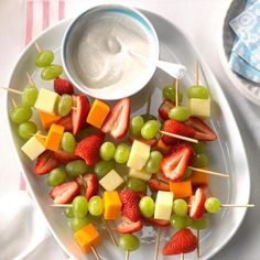 fruit and cheese skewers on a white plate with a bowl of yogurt