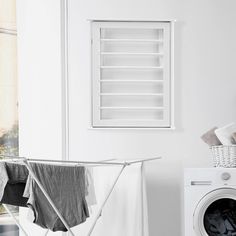 an ironing board next to a washing machine in a white room with open shutters