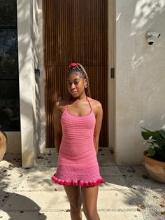 a woman standing in front of a door wearing a pink crochet mini dress