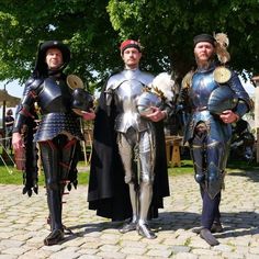 three men dressed in medieval armor standing next to each other on a cobblestone road