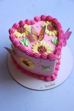 a pink heart shaped cake with flowers and butterflies on the top, sitting on a white plate