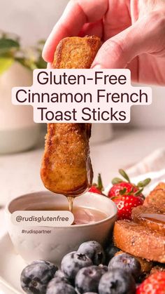 a person dipping gluten - free cinnamon french toast sticks into a bowl of blueberries and strawberries