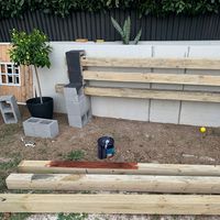 a wooden bench sitting in the middle of a yard next to a wall and potted plants