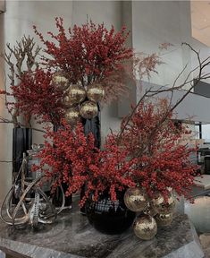 red flowers and branches in black vases on a marble table with gold ornaments around them