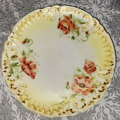 a plate with flowers painted on it is sitting on a tableclothed surface and has gold trim around the edge