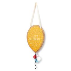 a yellow balloon with the words let's celebrate hanging from a string on a white wall