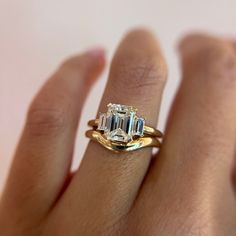 a woman's hand holding a ring with an emerald and diamond in the middle