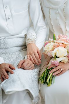 two people sitting next to each other with flowers in their hands and one person holding the bride's hand