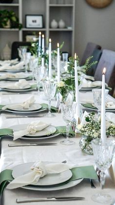 the table is set with white and green place settings, silverware, and candles