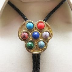 This cool Faux Gemstone bolo tie works for a woman with a sense of style. It is goldtone metal with small semiprecious cabochons in excellent condition. It measures 1 3/8ths inches tall by 1 3/8ths inches wide. It is placed on a brand new 36 inch long braided black leather string tie with  goldtone metal end caps. All pieces are in great condition.  This was handmade in our very own Montana rock shop, Rockin' JK Designs.  We will mail this to you in a lovely gift box for easy gift giving or safe Adjustable Southwestern Gold Jewelry, Vintage Jewelry With Adjustable Length For Formal Occasions, Vintage Formal Jewelry With Adjustable Length, Formal Lariat Jewelry With Adjustable Cord, Adjustable Multicolor Necklace For Formal Occasions, Vintage Lariat Jewelry With Sliding Knot, Gold Lariat Bolo Tie With Adjustable Length, Adjustable Gold Cabochon Necklace, Adjustable Metal Lariat Necklace For Formal Occasions