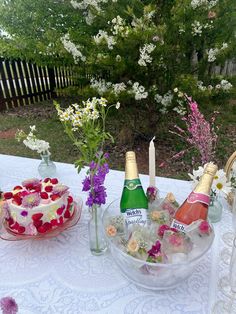 a table topped with two cakes covered in frosting next to wine bottles and flowers