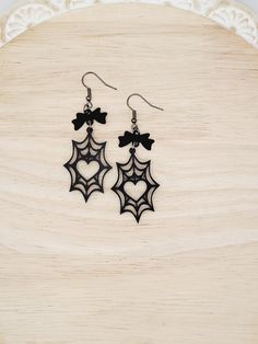 Black Spiderweb with Heart and Black Bow Dangle Earrings Add a touch of gothic elegance to your accessory collection with these Black Spiderweb with Heart and Black Bow Dangle Earrings. These stunning earrings are perfect for those who love unique, intricate designs with a hint of mystery. Features: - Materials: Intricately laser-cut from black matte acrylic, featuring a heart cut-out at the center of the spiderweb - Design: Delicate spiderweb with a charming heart detail, topped with a black alloy bow connector - Dimensions: Drop length of 2.75" and width of 1" - Hardware: Gunmetal black, hypoallergenic for sensitive ears Lightweight and comfortable, these earrings are perfect for adding a dark yet elegant touch to any outfit. Ideal for Halloween, themed parties, or everyday wear, these e Spooky Black Earrings For Party, Handmade Spooky Black Earrings, Spiderweb Design, Spooky Dangle Earrings, Spider Web Earrings, Novelty Black Halloween Earrings, Gothic Elegance, Heart Cut Out, Earrings Halloween