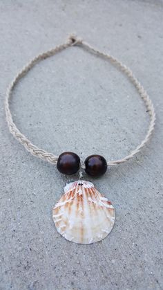 A brown, cream, and white seashell and dark red wood beads on braided cream hemp string. Drilling, twisting, and braiding is done by hand. Handmade Adjustable Brown Shell Necklace, Adjustable Brown Handmade Shell Necklace, Adjustable Handmade Brown Shell Necklace, Adjustable Brown Shell For Beach, White Braided Jewelry For Beach, White Braided Jewelry For The Beach, Brown Waxed Cord Beach Necklaces, Handmade Brown Beach Shell, Brown Waxed Cord Necklaces For The Beach