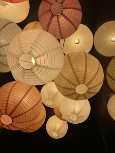 many lamps are hanging from the ceiling in different colors and shapes with lights on them